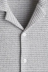 Camisa de manga corta color gris claro, de punto con textura de mezcla de algodón. Modelo con cuello abierto, tapeta lisa y bajo recto. Corte estándar para una silueta clásica y cómoda.