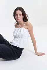 Top blanco con breteles finos, escote recto y corte peplum con frunces en la cintura.