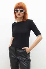 Sweater negro de tejido de punto con escote barco y mangas 3/4. Tiene detalle de ribete ondulado en color blanco en el escote y los puños.