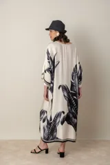 Vestido largo color natural con estampado de hojas de palmera en tonos verdes. Tiene corte amplio tipo túnica, cuello redondo, mangas tres cuartos, bolsillos laterales y ruedo con ribete.