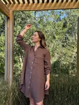 Vestido camisero blanco de lino, con cuello camisero, manga larga con botón para recoger, cierre frontal con botones de nácar, bolsillo en el pecho y diseño asimétrico más largo en la parte trasera.