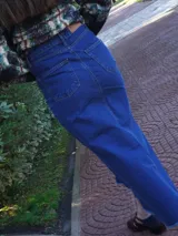 Falda larga de jean azul oscuro, corte amplio y recto, con abertura frontal y terminación desflecada en el ruedo. Presenta un pequeño parche de cuero marrón en la abertura lateral.