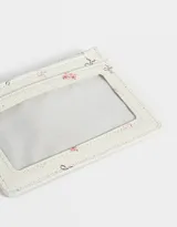 Tarjetero de cuerina color crema con estampado floral en tonos rosados, cierre superior con cremallera y ventana transparente para identificación.