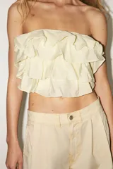 Top bandeau color crema con escote recto, hombros descubiertos y detalle de volantes en capas.