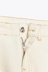 Pantalón de jean color crudo, de tiro alto y corte bootcut. Presenta cinturón fino del mismo tejido, bolsillos de parche en la parte trasera y cierre frontal con cremallera y botón.
