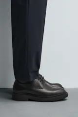 Zapato de vestir estilo derby, color negro, con capellada de cuero, horma redonda y suela de goma con volumen.