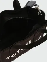 Bolso tote pequeño de lona color beige con estampado frontal en blanco con la leyenda "The Tote Bag Marc Jacobs". Tiene doble asa de mano y correa bandolera negra ajustable y extraíble.