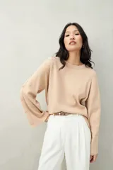 Sweater color beige de tejido de punto, con cuello redondo y mangas largas acampanadas con botones decorativos en los laterales.