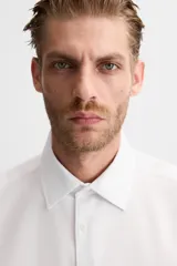 Camisa blanca de corte regular, cuello italiano, manga larga con puños abotonados y cierre frontal con botones.