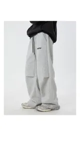 Pantalón deportivo gris jaspeado, corte ancho y holgado, con cordón ajustable en la cintura y detalle de etiqueta con texto en el bolsillo lateral.