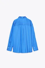 Camisa celeste con rayas verticales blancas, de corte oversize, cuello solapa, manga larga con puños y bolsillo de plastrón en el pecho.