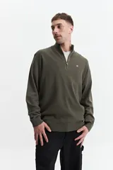 Sweater verde oliva de punto con cuello alto y cierre de medio cierre. Tiene puños y logo bordado en el pecho.