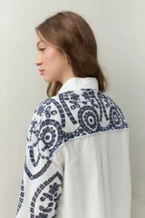 Camisa blanca de manga larga con bordado floral marrón, cuello clásico y cierre frontal con botones.