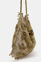 Mini bolso tipo saca de tela color beige con bordados florales y detalles de lentejuelas y mostacillas en tonos dorados y marrones. Posee asa de hombro hecha de mostacillas doradas y borde festoneado con mostacillas.