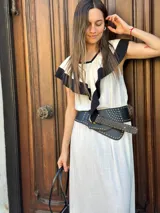 Vestido midi color crudo con detalles en negro en cuello, volados y ruedo. Incluye cinturón ancho negro con tachas y hebilla dorada.