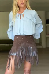 Minifalda marrón de cuero gamuzado, con tachas plateadas y flecos largos.