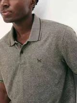 Polo de hombre color gris oscuro jaspeado, con cuello y puños de manga con ribete negro. Presenta un pequeño logo bordado en el pecho.