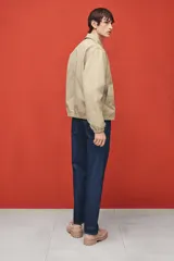 Campera color beige de denim rígido con cuello clásico, cierre frontal, bolsillos insertados al bies y un bolsillo interior. Elástico revestido en puños y bajo. Corte estándar y forrada.