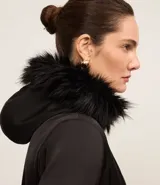 Campera parka negra con cuello alto, capucha con borde de piel sintética, cierre frontal con cremallera, bolsillos con cremallera y cinturón con hebilla.