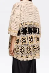 Cárdigan de algodón crochet color crema, con cuello camisero, manga corta y cierre frontal con botones. Presenta apliques de flores tejidas en negro y dorado. Corte oversize.