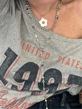 Set de tres collares plateados de diferentes largos. El más corto es tipo choker, el segundo tiene un dije de flor y el más largo es tipo corbatín con piedras de colores.