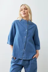 Camisa de jean celeste de corte recto, con cuello mao, mangas cortas y cierre frontal con botones.