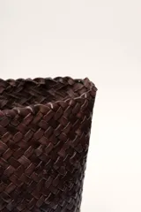 Bolso tipo tote de cuero vacuno, completamente trenzado a mano. El color es marrón oscuro, casi chocolate. Posee dos asas de hombro trenzadas.