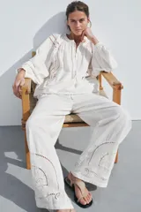 Pantalón de tiro medio color crudo, confeccionado en mezcla de algodón y lino, con cintura elástica ajustable con cordones, bolsillos laterales ocultos y detalle de bordados perforados a tono en el ruedo.