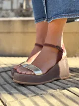 Sandalias de cuero con plataforma, color marrón con tira dorada sobre los dedos y tobillera marrón con hebilla.