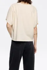 Remera color crema de corte holgado y mangas cortas con detalle de pinzas en los hombros.