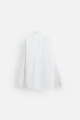 Camisa blanca de algodón, corte regular fit, cuello italiano, manga larga con puños abotonados y cierre frontal con botones.