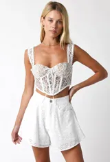 Corset blanco de encaje con tirantes y cordones ajustables en el frente.