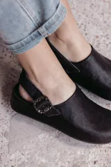 Zuecos negros de cuero con textura de pelo, diseño cerrado con hebilla lateral y tira ajustable en el talón.