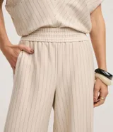 Pantalón de mujer de tiro alto, corte wide leg, color beige con finas rayas verticales en tono oscuro. Presenta cintura elástica fruncida y caída fluida.