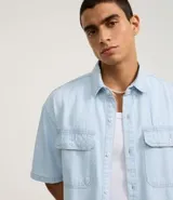 Camisa masculina de jeans celeste con estampa de rayas verticales, corte boxy, cuello inglés, manga corta, cierre abotonado y bolsillos frontales.