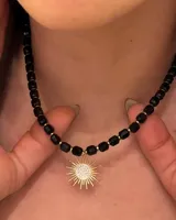 Collar corto de cuentas facetadas negras con detalles dorados y dije de sol dorado con centro de circonias.