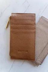 Tarjetero de cuero color rosa pálido con cierre de cremallera dorada y múltiples ranuras para tarjetas.