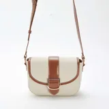 Bolso bandolera de lona color beige con detalles en cuero marrón. Tiene correa larga ajustable y cierre con hebilla dorada.
