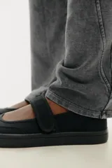 Zapato plano tipo bailarina en tejido color negro. Detalle de pespunte en el cuerpo, tira con adhesivo ajustable, suela engomada y acabado en punta redonda.