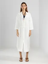 Camisa larga blanca de lino italiano, con cuello clásico, mangas 3/4, silueta fluida, dobladillo curvado en las costuras laterales y bolsillos discretos.