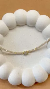 Pulsera elástica de cristalitos facetados color beige, con cuentas doradas y dije de estrella con circonitas.