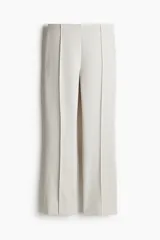Pantalón tobillero color crudo de sarga con tiro alto, elástico oculto en la cintura y cierre lateral oculto. Piernas ajustadas con bajo levemente acampanado y pliegues frontales.