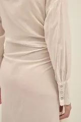 Vestido camisero largo color crema, de algodón, con cuello clásico, mangas largas con puños abotonados, cierre frontal con botones nacarados y lazo para atar en la cintura.