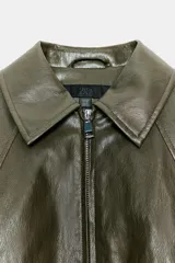 Chaqueta estilo bomber de efecto piel en color verde oliva, con cuello solapa, cierre frontal con cremallera, mangas largas y bajo con acabado elástico.