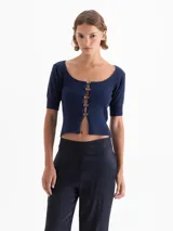 Top corto de punto acanalado color azul marino, con escote redondo, manga corta y cierre frontal con tres ganchos decorados con piedras.
