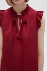 Blusa sin mangas color crudo con cuello con lazo y volados en los hombros.