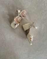 Sandalia de cuero vacuno en tono dorado, con taco de 8 cm y tiras ajustables.