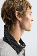 Sudadera gris de corte holgado, con cuello polo negro, cierre frontal de tres botones y mangas largas con puños acanalados.