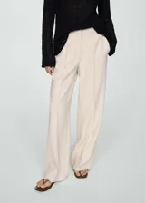 Pantalón de vestir color beige, de corte wide leg, tiro medio, con pinzas delanteras, bolsillos laterales y cierre frontal oculto con botón, gancho y cremallera.