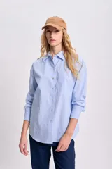 Camisa celeste con rayas verticales blancas, de corte clásico, con cuello camisero, manga larga y bolsillo en el pecho.